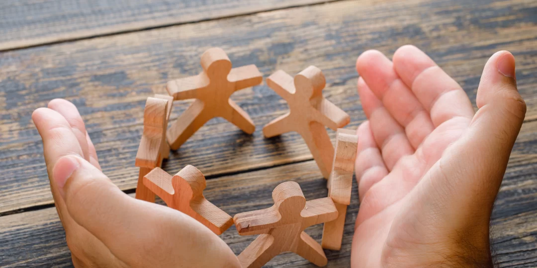 business-success-concept-wooden-table-top-view-hands-protecting-wooden-figures-people-1080x540.webp